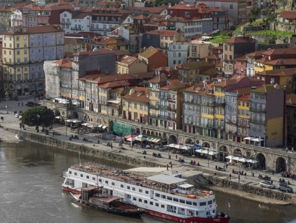 Colourful houses along a riverside street with boats in the river and lively street life, porto,