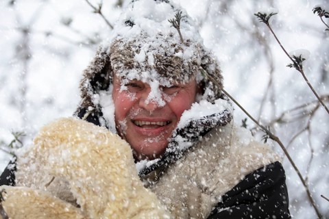 A frozen man covered in winter snow smiles and looks at the camera. The first snow has fallen. A
