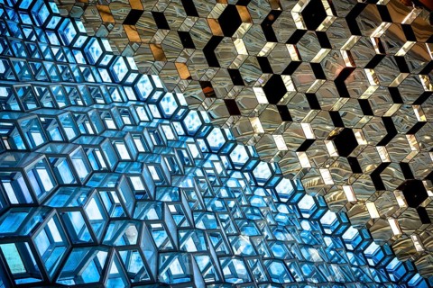 Compact geometric patterns in a glass architecture reflecting blue and gold tones, Harpa Concert