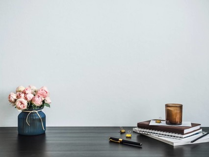 Home office desk with copy space. Pink flowers, scented candle, stack of books on black tabetop.
