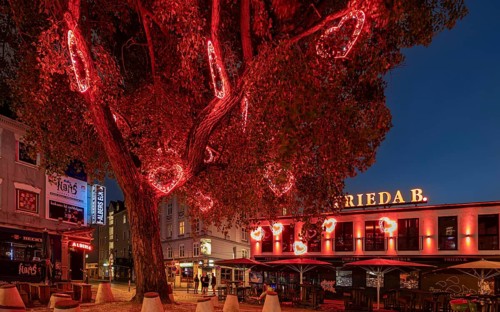 A tree with red heart-shaped lights decorates a lively urban scene at night, Hans-Albers-Platz, St.
