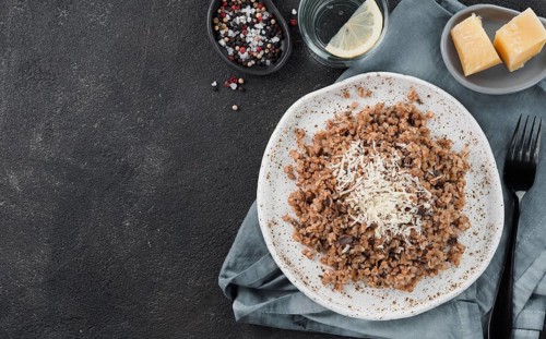 Buckwheat risotto with dried mushrooms served parmesan cheese in craft plate on black cement