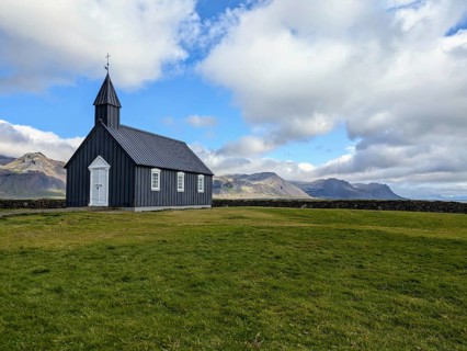 Isolated black church on grassland with mountains in the background under a cloudy sky. Iceland