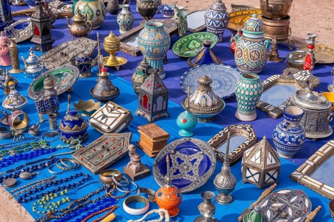 A colorful Moroccan market scene along a bustling street, with vendors selling spices, textiles,