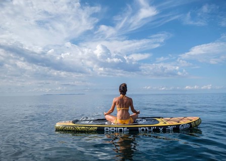 Woman practicing yoga on a surfboard under a dramatic sky, Estalella, coast of Llucmajor, Majorca,