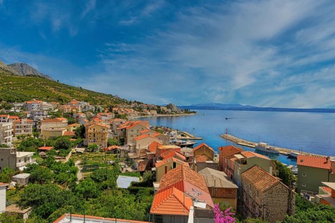 Coastal town with red roofs and views of the sea and distant mountains under a blue sky, Makarska
