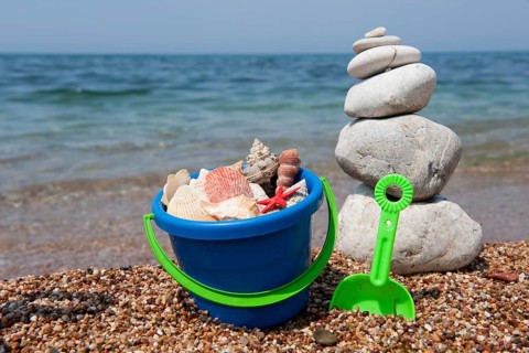 Shells on the beach in colorful bucket with stacked pebbles
