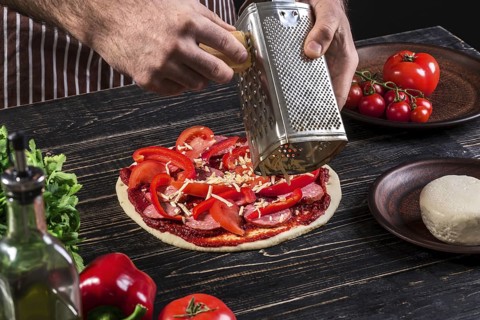 Cook in the kitchen putting the ingredients on the pizza on an old wooden background. Pizza concept