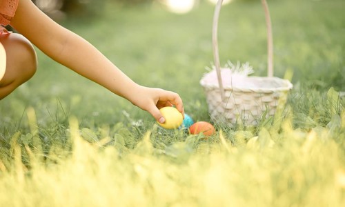 Little cute girl holding basket with colorful painted eggs on Easter egg hunt in park