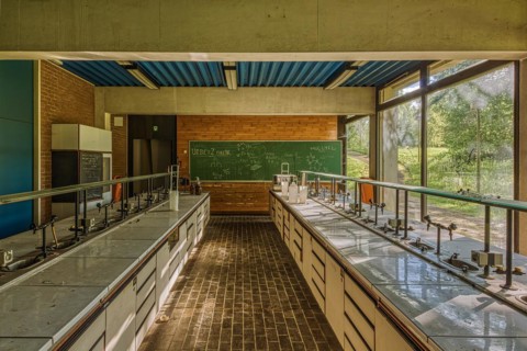 Empty classroom with view of green trees through windows, blackboard and laboratory tables,