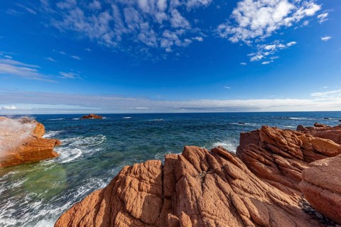 Coastal landscape with red rocks and surf in blue sky and sunshine, Spiaggia di Cala E'Luas,