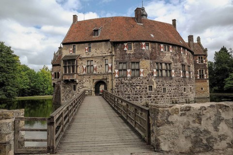 Wide bridge leads to a historic castle with moat, surrounded by nature, cloudy sky, lüdinghausen,