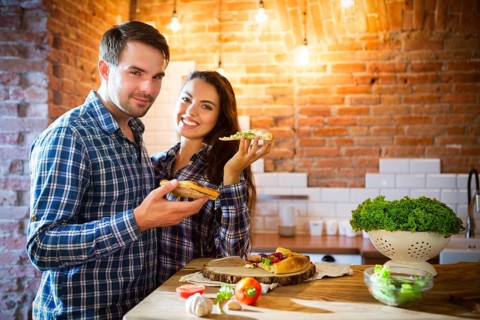 Young smiling couple eating homemade pizza together at kitchen