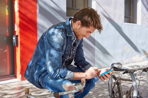 Young man using smartphone in a bicycle with jeans denim outdoor