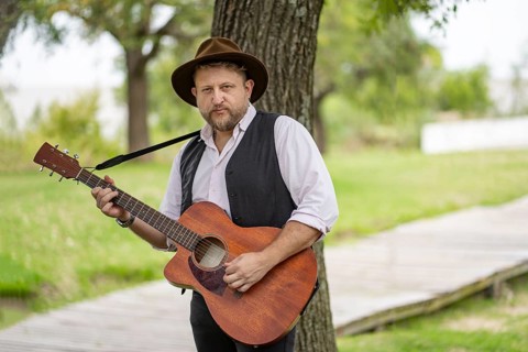 Musician posing for the camera while playing guitar in a park