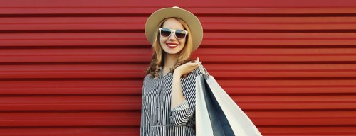 Stylish beautiful happy smiling young woman posing with shopping bags in summer straw hat on red