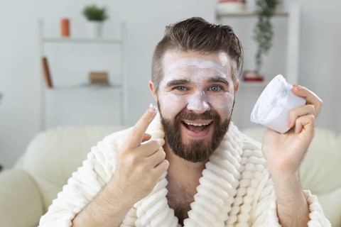 Bearded guy applying anti-wrinkle cream on his face. Skin care and spa for man concept