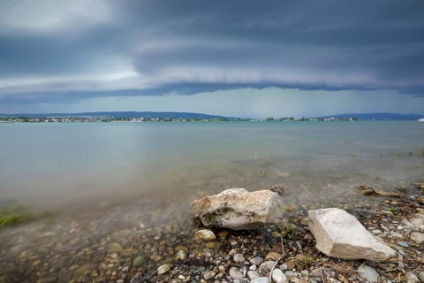 Stormy sky over a calm lakeshore with stones and clear water, Allensbach, Untersee, Lake Constance,
