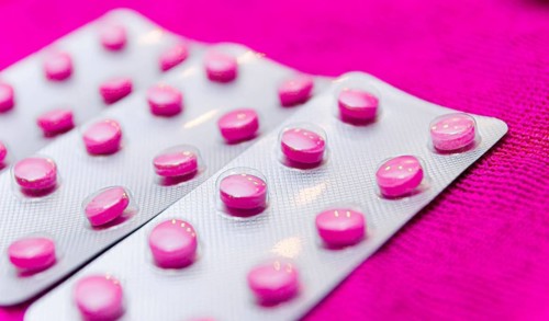 Pink pills in a blister on a pink background close up