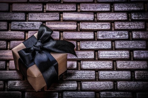 Wrapped present box with black ribbon on wicker wooden mat