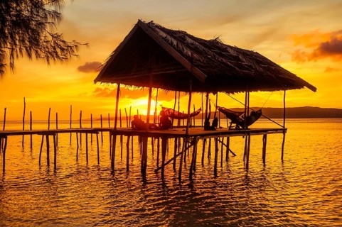 Native people relaxing in hammocks on wooden jetty during sunset on Kri island, Raja Ampat, West