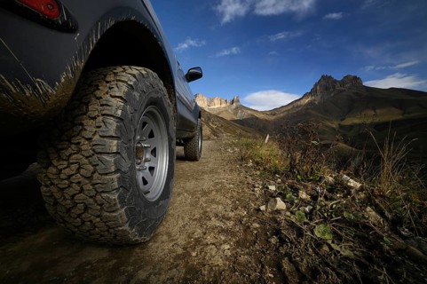 Close-up A large off-road all-terrain car wheel stands on a rough road in the mountains against the