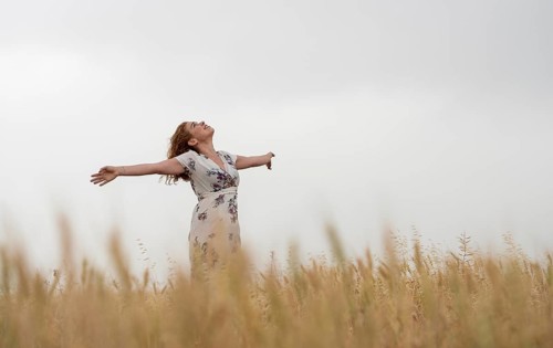 Happy woman in a floral dress stands amidst golden wheat, enjoying the serene landscape