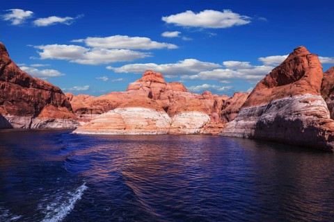 The foamy trace from powerboat crosses emerald waters. Hills from red sandstone surround the lake.