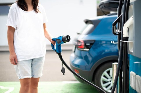 Woman charge her Electric car on gas station. Blue car and electric plug for charging. Ecology