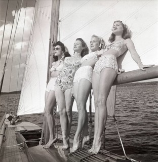 1940s sailing boat. Four young women are standing and leaning against the sails of the boat and