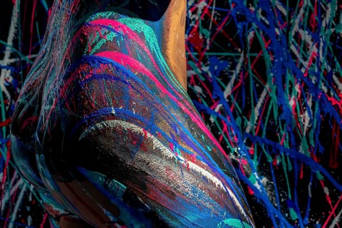 A model poses gracefully, her body adorned in vibrant body paint, with brilliant, sweeping strokes