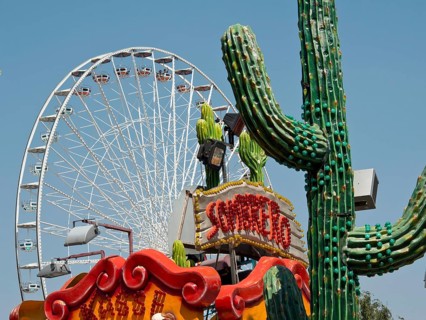 Colourful amusement park with a large Ferris wheel and decorative cacti under a clear sky, Vienna,