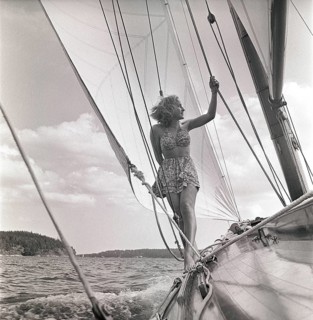 1940s sailing boat. A young woman is aboard a fashionable sailing boat and is standing on deck when