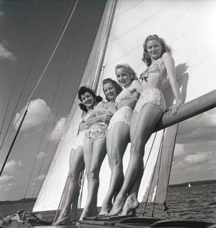 1940s sailing boat. Four young women are standing and leaning against the sails of the boat and