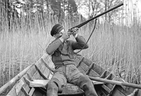 In the 1930s. A man sits in a rowing boat and aims his rifle upwards to shoot ducks. Sweden 1939.