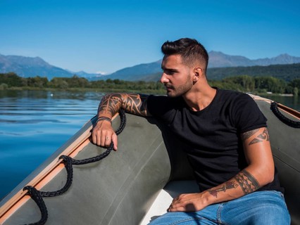 Portrait of young handsome man with tattooed body looking at camera sailing in boat