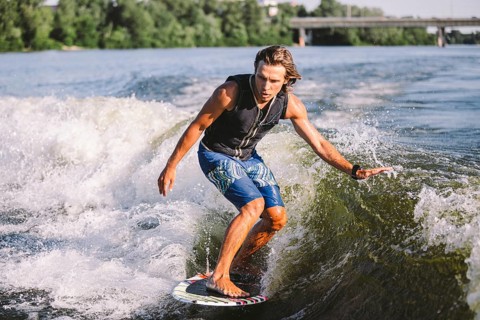 Young athletic man with long hair wakesurfing on waves of river in sunny summer weather. Ttheme