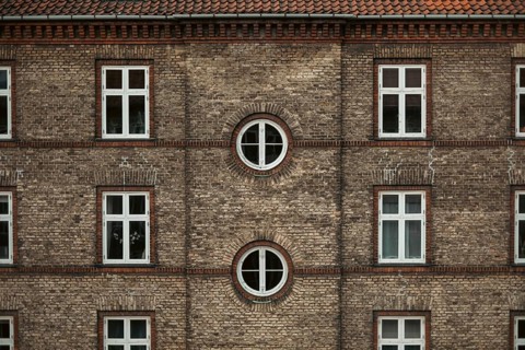Symmetrical brick building façade with square and round windows, displaying traditional