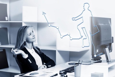 Young pretty business woman sitting at the desk with computer in blue office