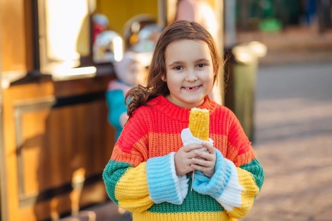 Caucasian little cute girl eating delicious tasty corn on the cob in city park