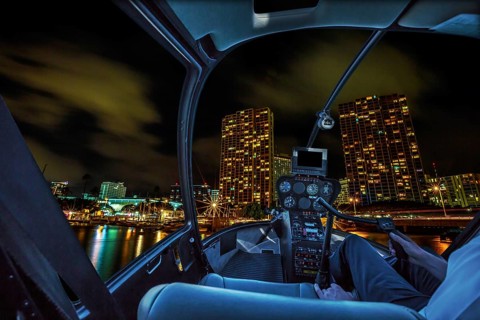 Helicopter cockpit flies in Honolulu skyline by night, Oahu, Hawaii, with pilot arm and control