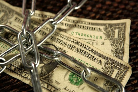 One Dollar notes in chains studio shot over brown background