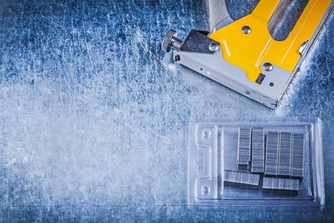 Yellow stapler gun chrome staples on scratched metallic background