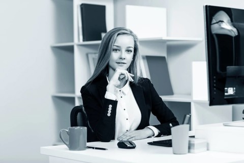 Young pretty business woman sitting at the desk with computer in blue office