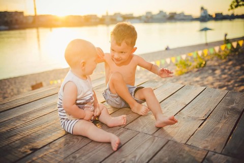Two little boys sitting on the pier on the river bank. Concept of friendship and fraternity. Sunny
