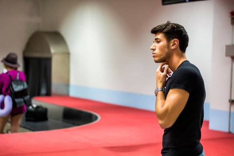 Young man standing in the airport waiting for his baggage at luggage claim belt