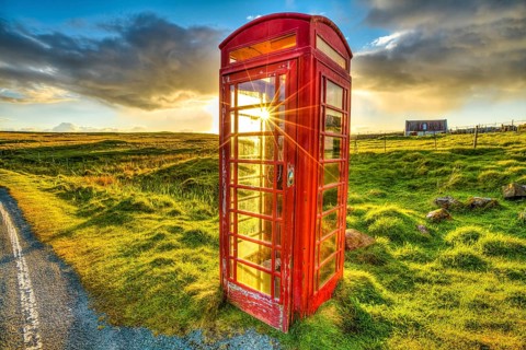 Urban red telephone box in the middle of a green countryside. Concept for synergy between modern
