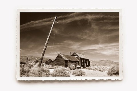 Lonely wooden house in Bodie, in front of it a crooked lamp post. Dry grass and undergrowth in the