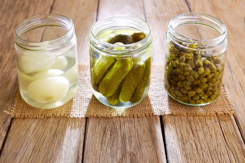 Bottled pickles as capers onion and cucumbers in wooden table