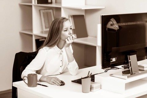 Young pretty business woman sitting at the desk with computer in blue office